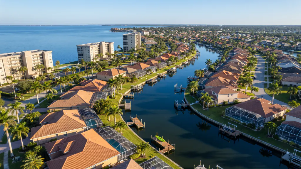 Aerial of a Florida canal neighborhood with tile-roof homes, docks and a few condo buildings by the water.